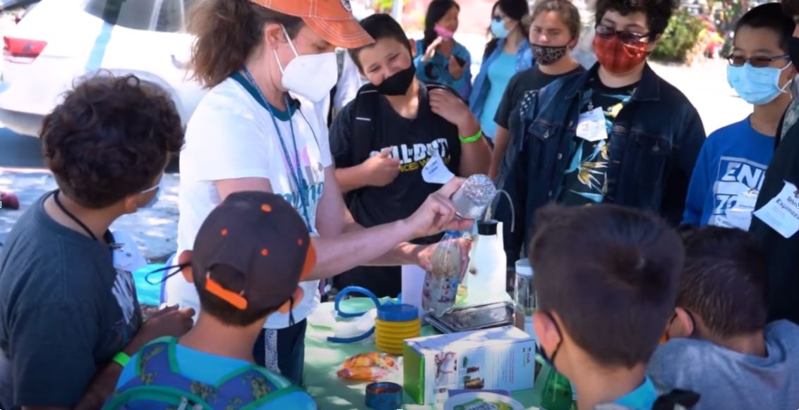 A hands-on community science demonstration for a group of students at an outdoor table.